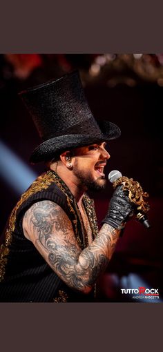 a man with tattoos and a top hat on holding a microphone in his right hand