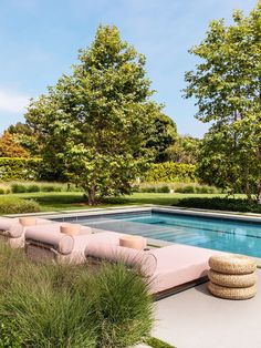 an outdoor lounge area next to a swimming pool with grass and trees in the background