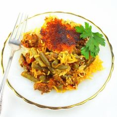 a white plate topped with green beans and rice next to a fork on top of a table