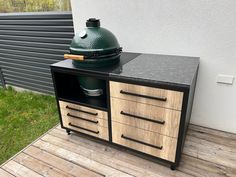 a big green egg sitting on top of a wooden table next to a grill outside