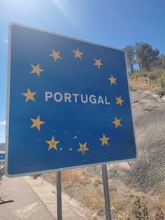 a blue sign with yellow stars on it that says portugal next to a dirt road