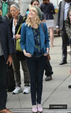 a woman standing in front of a crowd of people on the sidewalk with her eyes closed