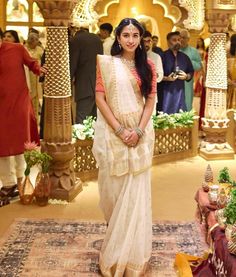 a woman in a white sari standing on a rug with other people around her