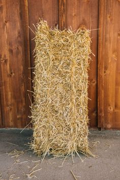 a pile of hay sitting on top of a sidewalk next to a wooden wall and fence