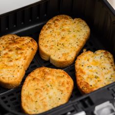 four pieces of bread sitting in an air fryer with cheese and herbs on top