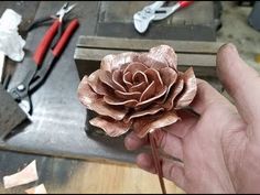 a person is holding a flower in their hand and tools are on the table behind them