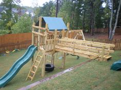 a wooden play set in the backyard with a slide and climbing frame attached to it