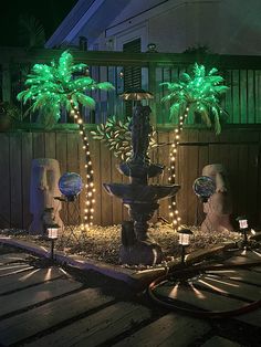 a lighted fountain in the middle of a yard with palm trees and lights around it