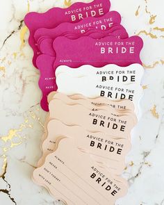 pink and white paper tags with words on them sitting on a marble countertop next to gold foil