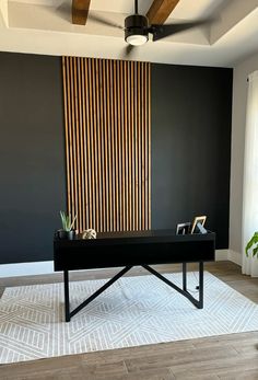 a black desk in front of a wall with wooden slats on it and a plant next to it