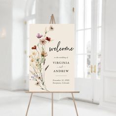 a welcome sign with wildflowers on it in front of a white wall and windows