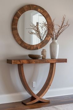 a wooden table with a mirror and vase on it next to a white wall in a room