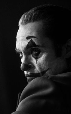 a man with his face painted as the joker in black and white, looking off into the distance