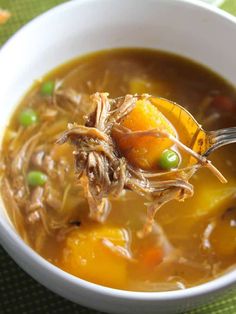 a white bowl filled with soup on top of a green place mat and a spoon