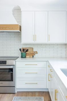 a kitchen with white cabinets and gold trim on the counter tops, along with a silver stove top oven