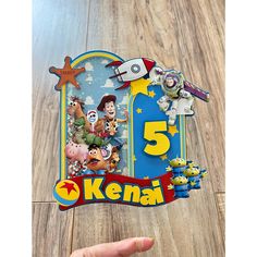 a hand holding up a sticker with the number five on it and characters from toy story