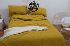 a bed with yellow sheets and pillows next to a white chair in a room that has hardwood floors