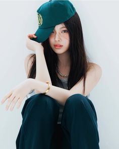 a woman sitting on the ground wearing a green hat and blue pants with her hand resting on her head