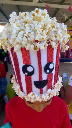 a child wearing a popcorn bucket hat with eyes and nose painted to look like a movie character