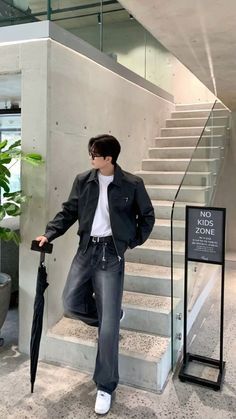 a man holding an umbrella while standing in front of a stair case with a sign on it