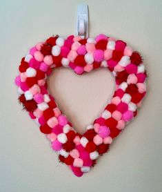 a heart shaped wreath with pom - poms hanging on a wall in the shape of a heart