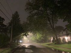 an empty street at night with the lights on and trees in the foreground,