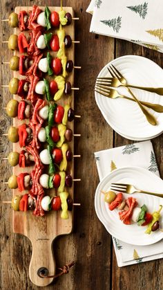 a wooden table topped with white plates filled with veggie skewers and forks