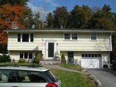 a car parked in front of a two story house with white siding and trees behind it