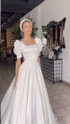 a woman in a white wedding dress standing next to a mirror and looking at the camera