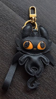 a black cat keychain with an orange eyes on it's face and ears