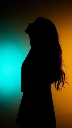 a woman standing in front of a green and yellow light with her hair blowing in the wind