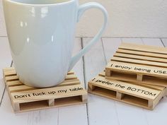 a white coffee cup sitting on top of a wooden crate next to two coasters