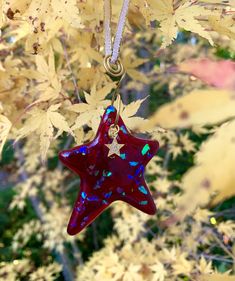 a red glass star ornament hanging from a tree with leaves in the background