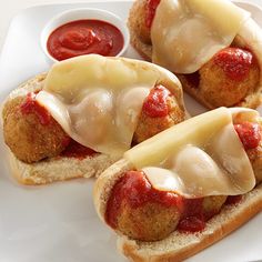 three hot dogs with cheese and ketchup on a white plate next to dipping sauce