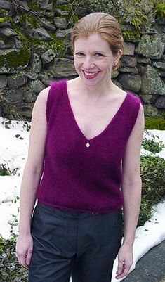 a woman standing in front of a stone wall with snow on the ground behind her