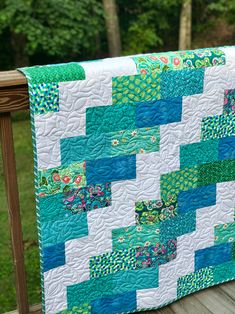 a blue and green quilt is hanging on a wooden rail near some trees in the background