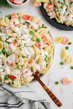 pasta salad with shrimp and peas in a bowl on a white table next to two plates