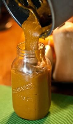 a person pouring mustard into a glass jar