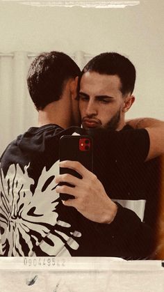 two men embracing each other while taking a selfie with their cell phone in front of them