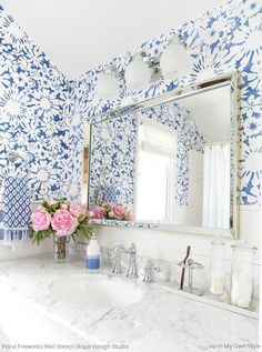 a blue and white bathroom with flowers on the counter top, large mirror over the sink