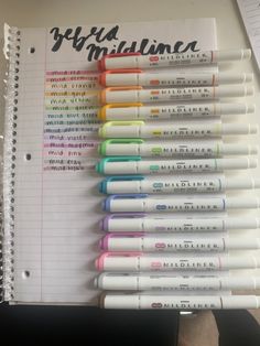 a bunch of pens sitting on top of a white paper next to a notebook with writing