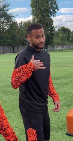 a man in black and orange tracksuits standing on a field with an orange object