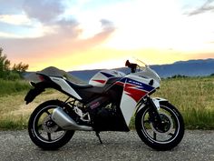 the motorcycle is parked on the side of the road in front of grass and mountains