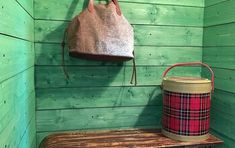 a wooden bench with a bag hanging from it's back and a bucket next to it