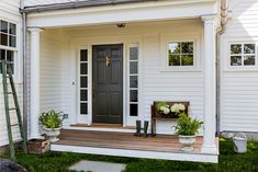 the front porch of a white house with potted plants