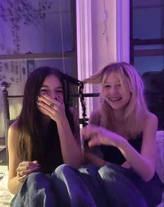 two women sitting on a bed and one is holding her face up to the camera