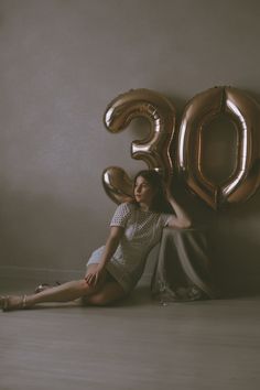 a woman sitting on the floor with balloons in front of her, posing for a photo