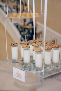 cookies and milk are arranged in small cups on a clear tray with white sticks sticking out of them