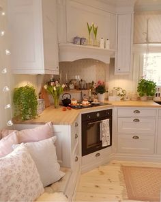 an instagram photo of a kitchen with white cabinets and pink pillows on the floor