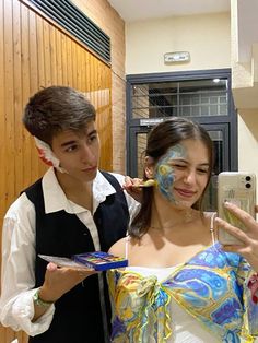 two people with face paint on their faces and one holding a cell phone in the other hand